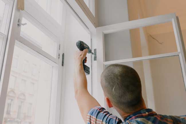 person holding a drill to a window pane